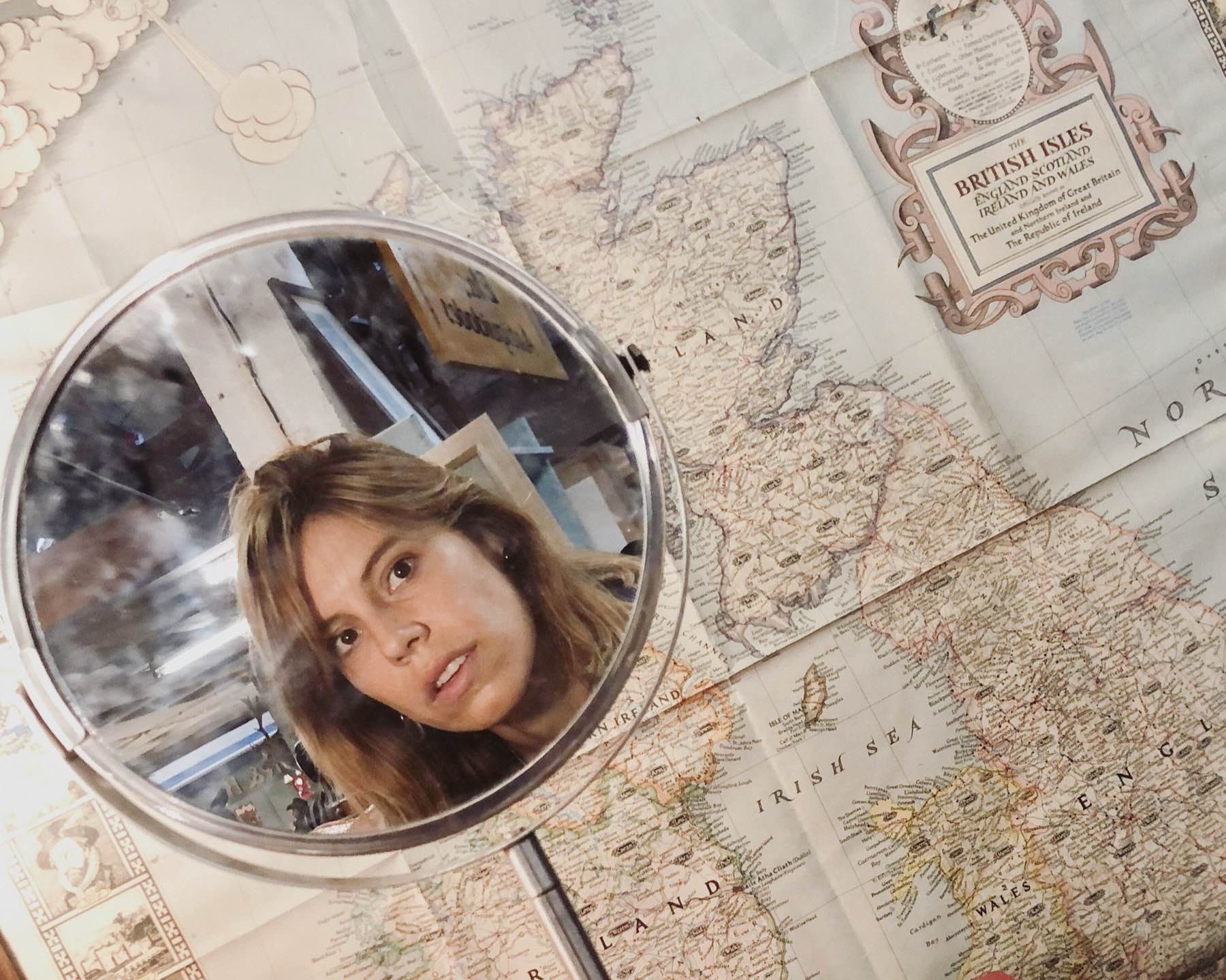 Overhead selfie taken in a small round mirror, held above an antique map of the British Isles