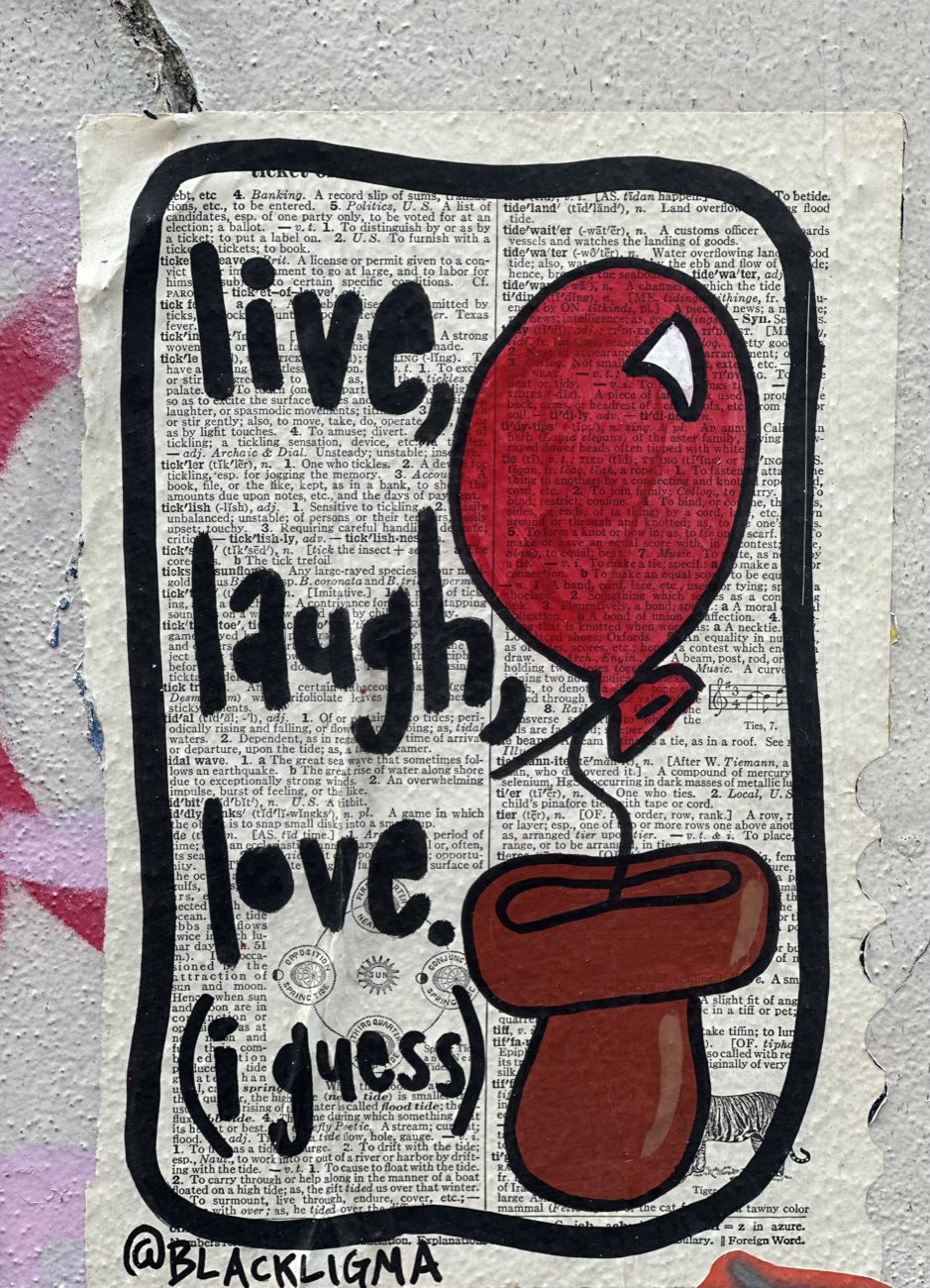 Street art on a dictionary page pasted to a wall: hand-lettered words 'live, laugh, love. (i guess)' next to a red balloon rising from a brown mushroom